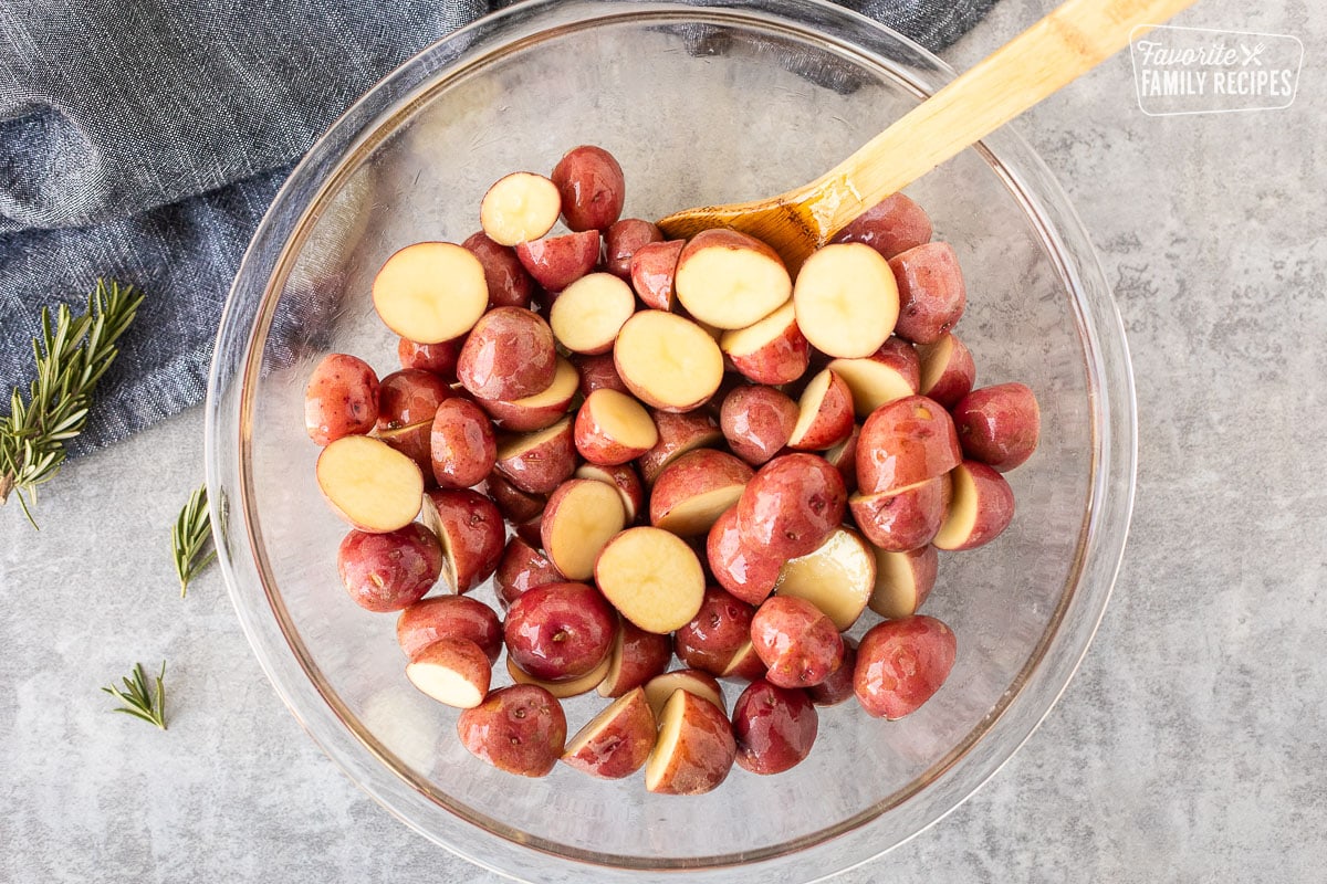 Mixing bowl with cut red potatoes tossed in olive oil and wooden spoon.