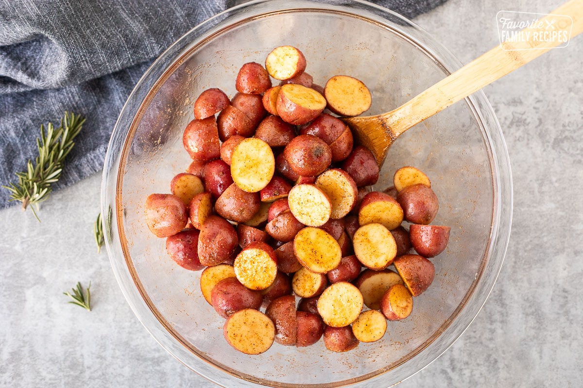 Glass mixing bowl with cut red potatoes, oil and seasoning.