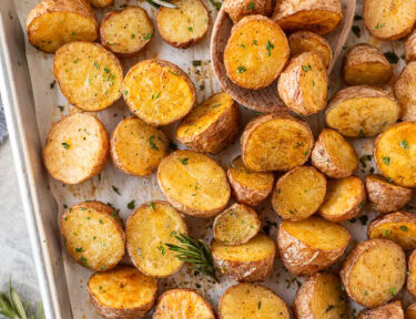 Roasted red potatoes on a baking dish with a wooden spoon.