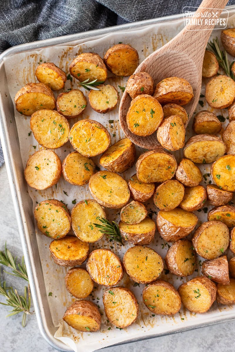 Roasted red potatoes on a baking dish with a wooden spoon.