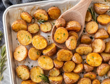 Roasted red potatoes on a baking dish with a wooden spoon.