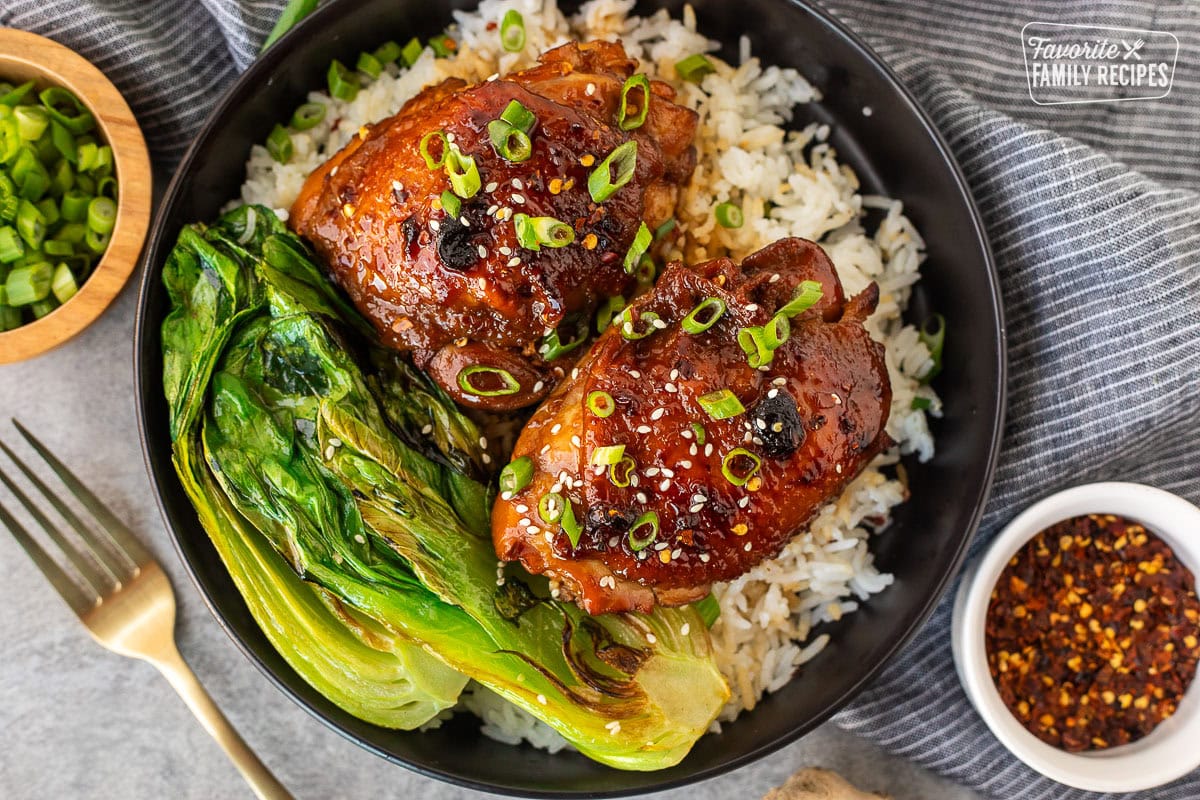 Shoyu chicken on a plate over rice with fresh sliced green onion, sesame seeds and bok choy.