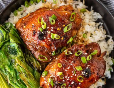 Shoyu chicken on a plate over rice with fresh sliced green onion, sesame seeds and bok choy.