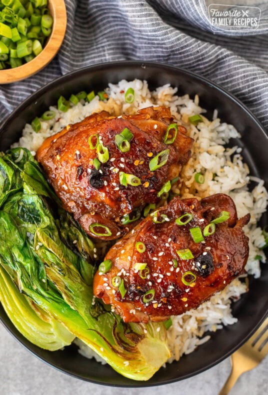 Shoyu chicken on a plate over rice with fresh sliced green onion, sesame seeds and bok choy.