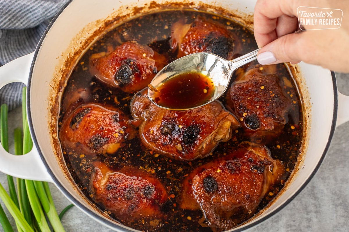 Pouring sauce with a spoon over Shoyu chicken and a Dutch oven.