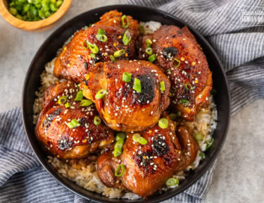 Plate with white rice and five pieces of Shoyu chicken topped with fresh slices of green onion and sesame seeds.