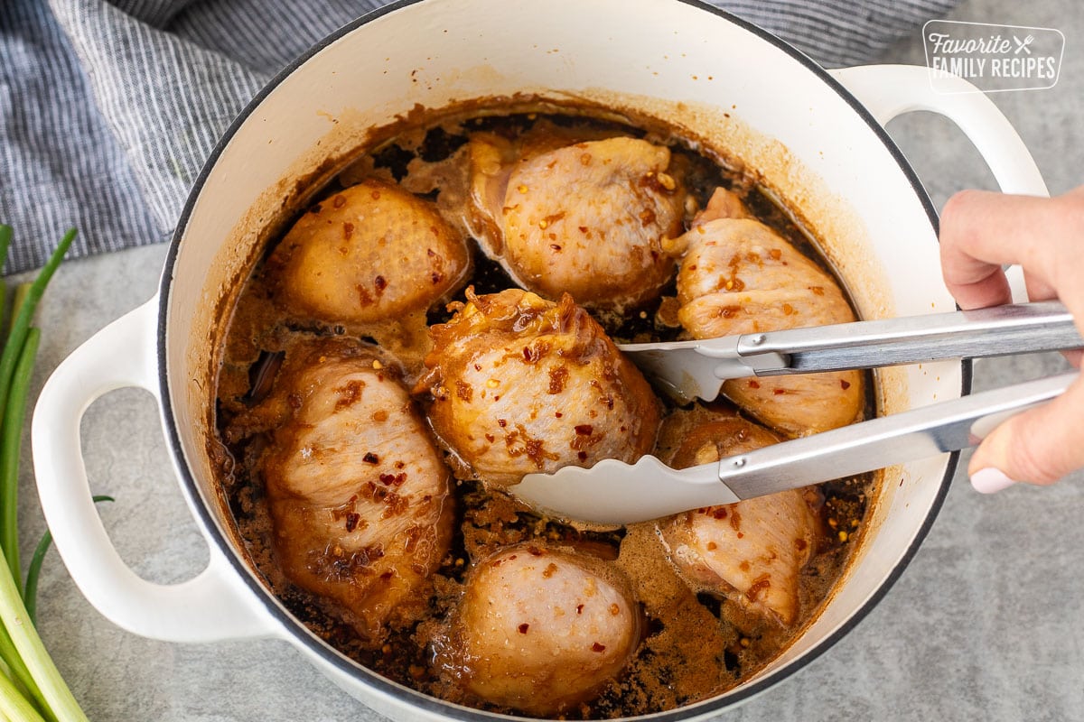 Using tongs to flip over Shoyu chicken in a Dutch oven.