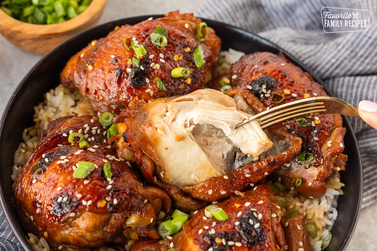 Fork tearing off a piece of chicken thigh from a cooked piece of Shoyu Chicken.