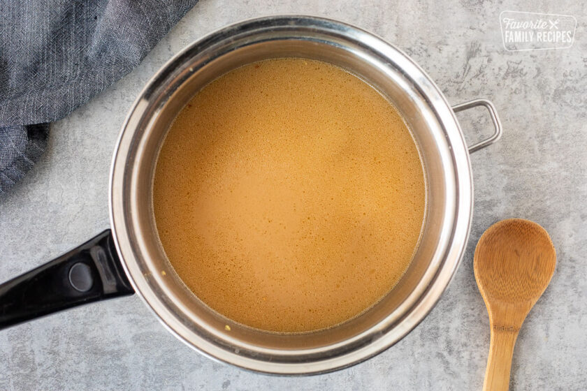 Sauce pan with Ramen broth and a wooden spoon on the side.