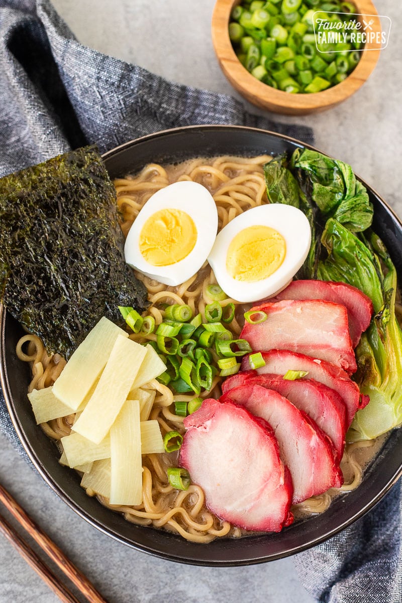 Bowl of Shoyu Ramen topped with barbecue pork, bok choy, sliced green onion, bamboo, boiled eggs sliced in half and seaweed sheets.