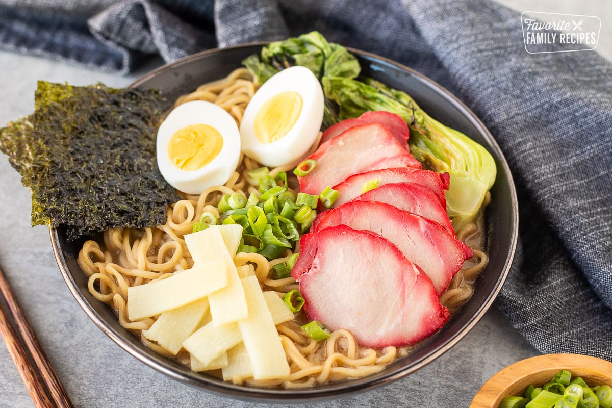 Bowl of Shoyu Ramen topped with barbecue pork, bok choy, sliced green onion, bamboo, boiled eggs sliced in half and seaweed sheets.