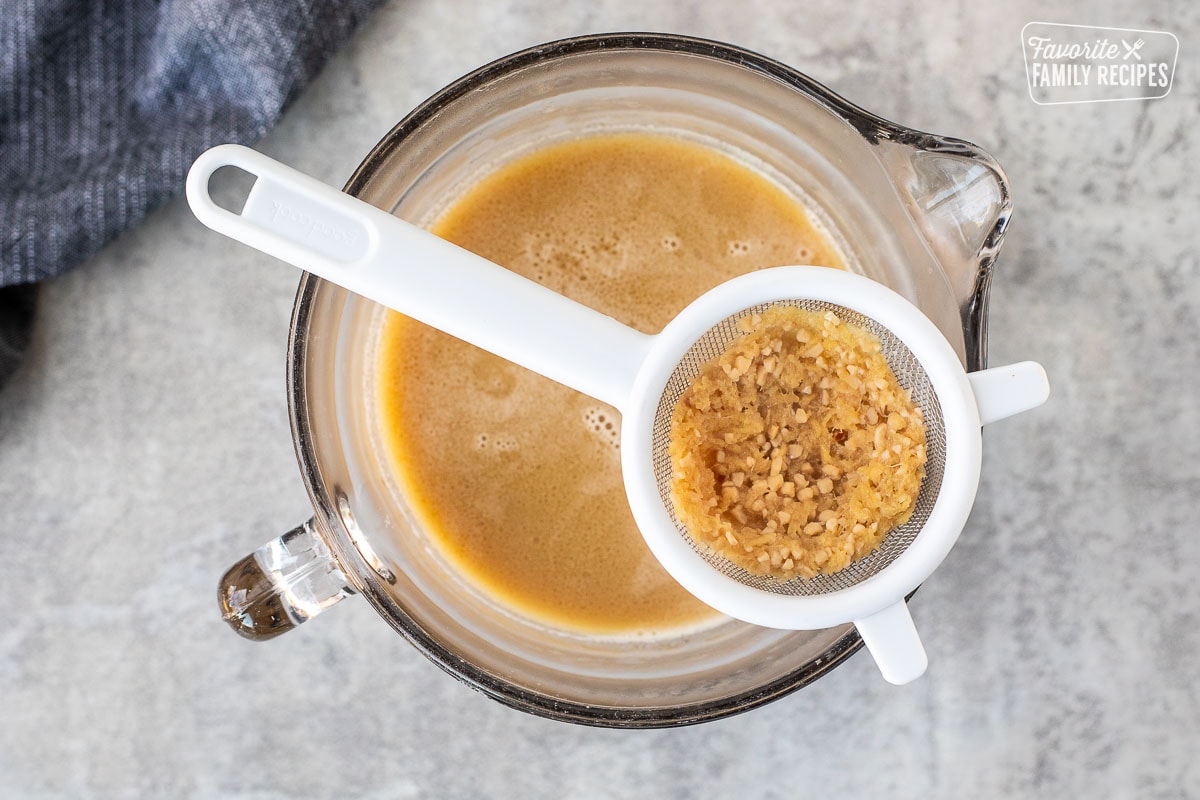 Strainer with garlic and ginger over a bowl of Ramen broth.