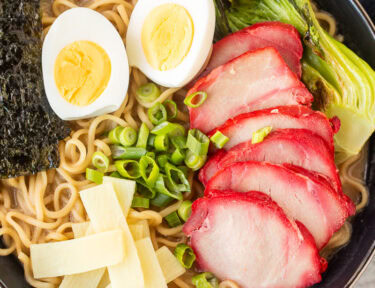 Bowl of Shoyu Ramen topped with barbecue pork, bok choy, sliced green onion, bamboo, boiled eggs sliced in half and seaweed sheets.