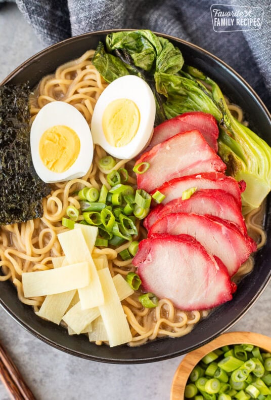 Bowl of Shoyu Ramen topped with barbecue pork, bok choy, sliced green onion, bamboo, boiled eggs sliced in half and seaweed sheets.