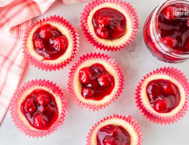 An overhead shot of six mini cherry cheesecakes next to a jar of cherries.