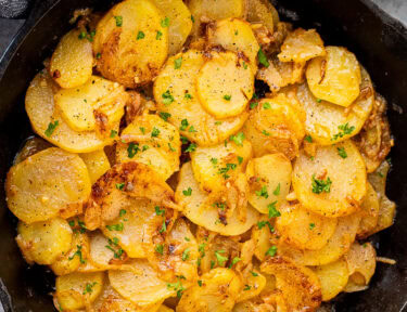 Skillet of Smothered Potatoes garnished with fresh parsley.