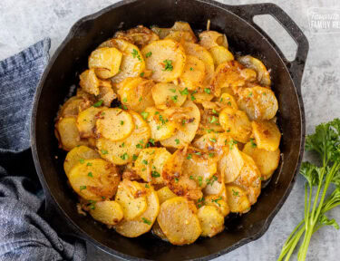 Skillet of Smothered Potatoes garnished with fresh parsley.