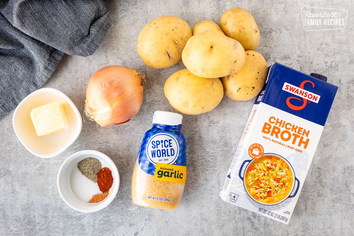 Ingredients to make smothered potatoes including yellow potatoes, onion, garlic, chicken broth, butter and seasonings.