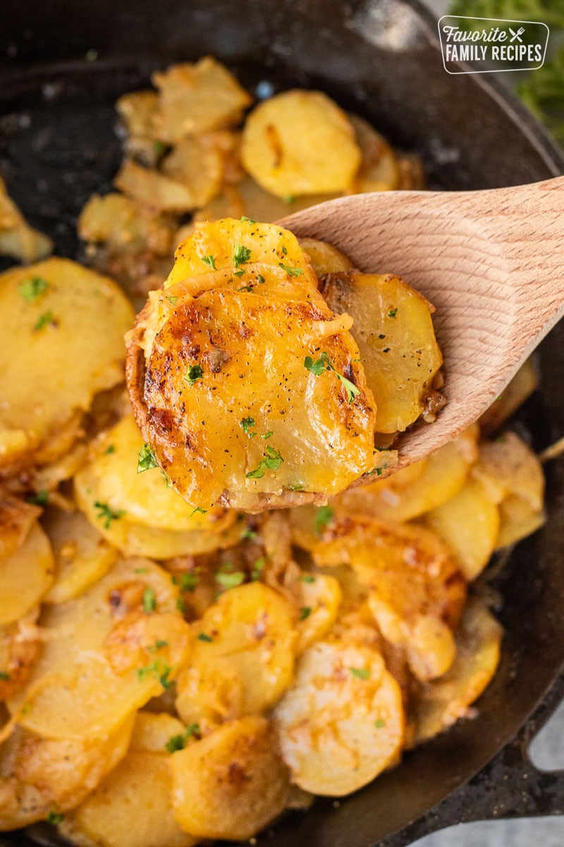 Wooden spoon of Smothered Potatoes garnished with fresh parsley.