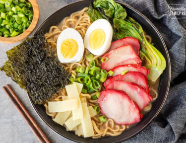 Bowl of Shoyu Ramen topped with barbecue pork, bok choy, sliced green onion, bamboo, boiled eggs sliced in half and seaweed sheets.