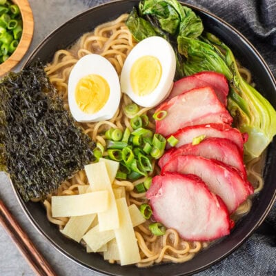 Bowl of Shoyu Ramen topped with barbecue pork, bok choy, sliced green onion, bamboo, boiled eggs sliced in half and seaweed sheets.