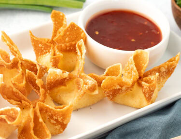 Plate of crispy, golden cream cheese wontons with a side of sweet and sour sauce.