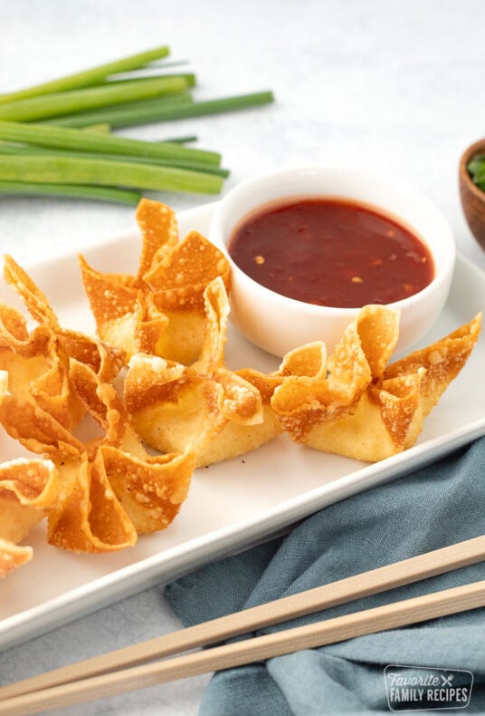 Plate of crispy, golden cream cheese wontons with a side of sweet and sour sauce.