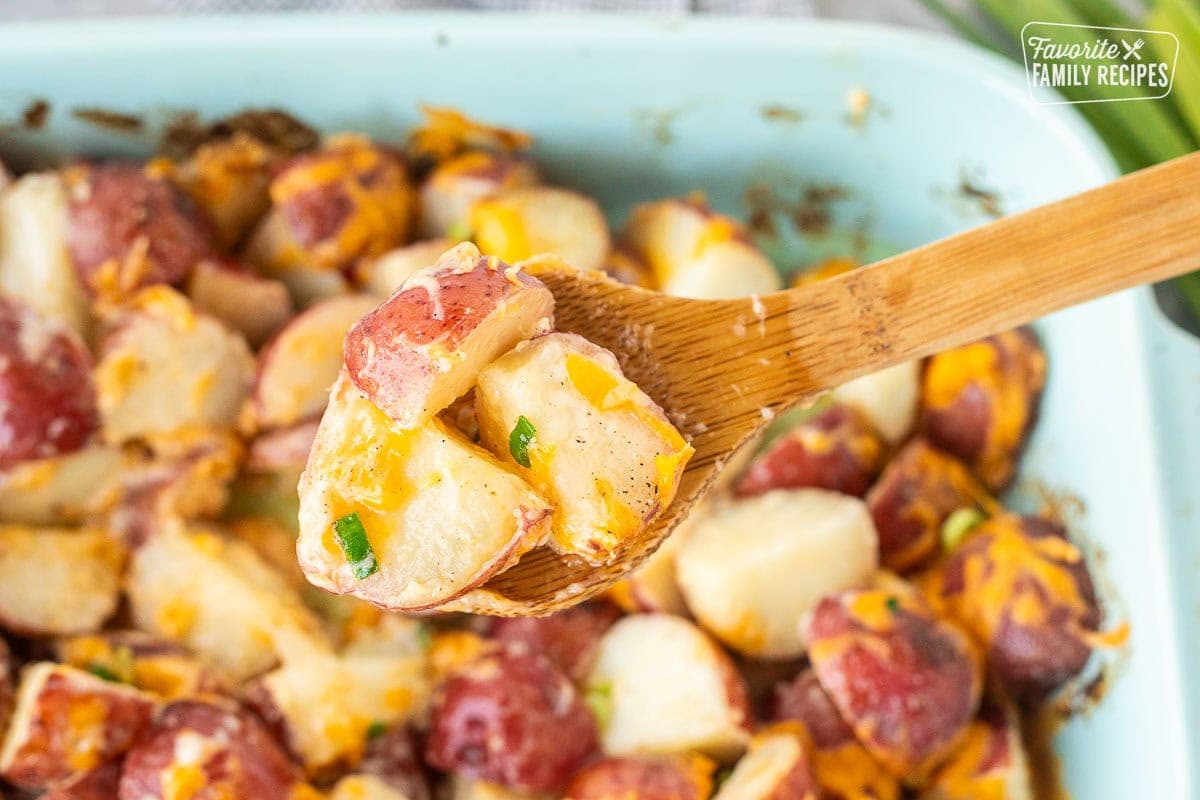 Wooden spoon with cheesy Ranch potatoes over a baking dish.