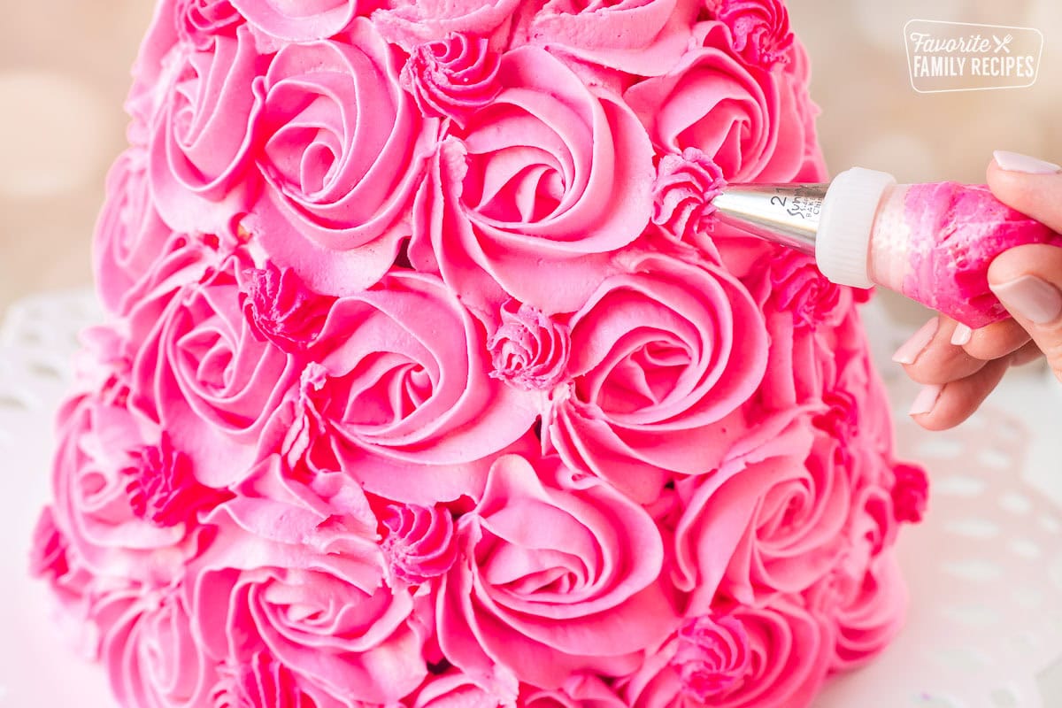 Pink frosting being piped into rosettes onto a Barbie Cake to make the dress part of the cake.