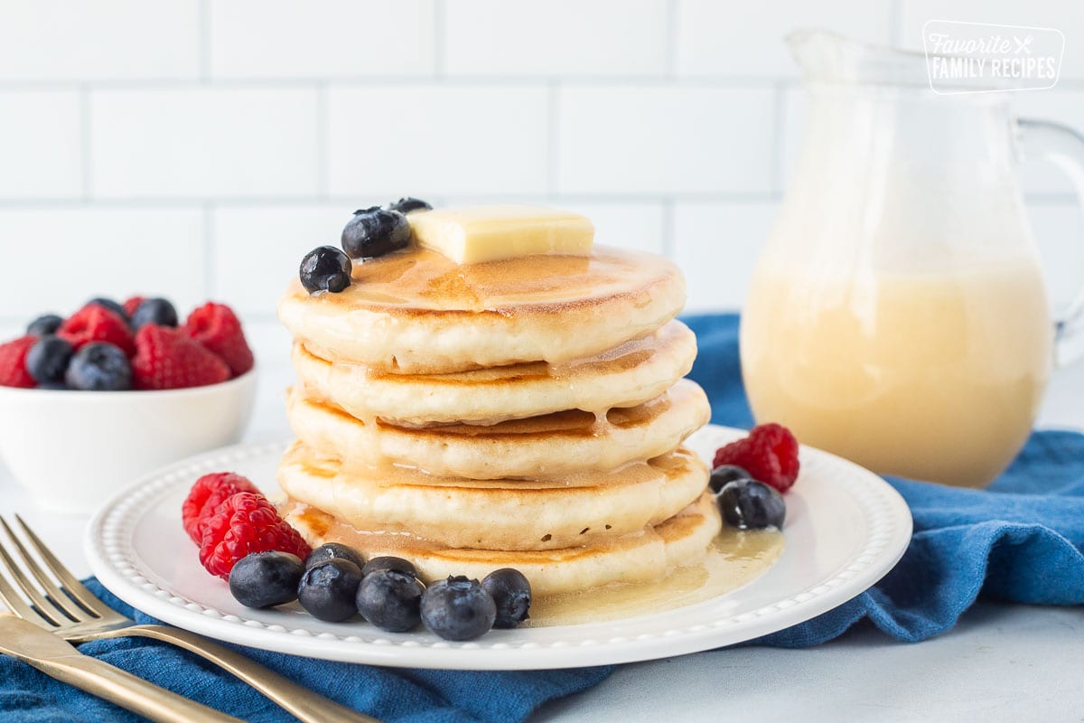 Stack of buttermilk pancakes on a plate topped with homemade buttermilk syrup, butter, blueberries and raspberries.