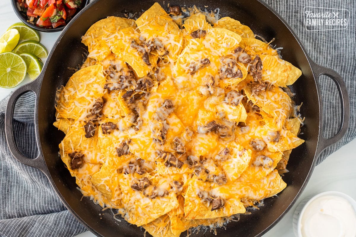 Large skillet with melted cheese on top of card Asada and tortilla chips chips.