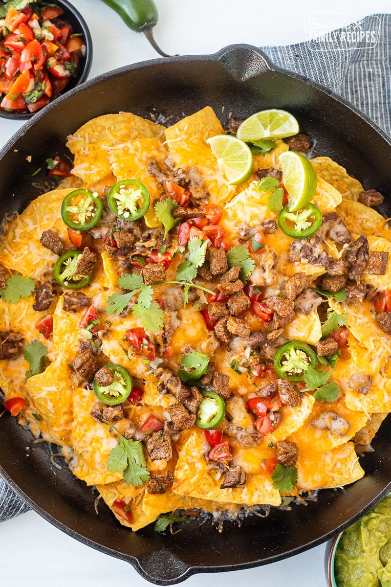 Carne Asada nachos with toppings including sliced jalapeños, pico de gallo, cilantro, and lime wedges.