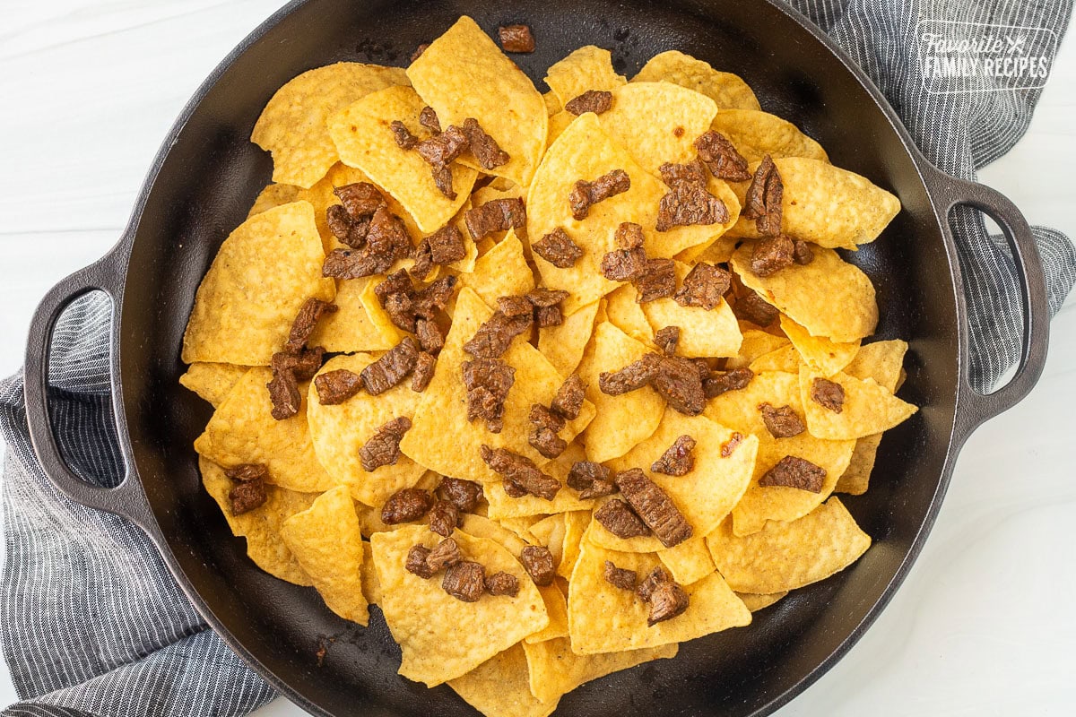 Large skillet with tortilla chips and pieces of Carne Asada on top.