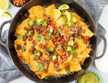 Carne Asada nachos with toppings including sliced jalapeños, pico de gallo, cilantro, and lime wedges.