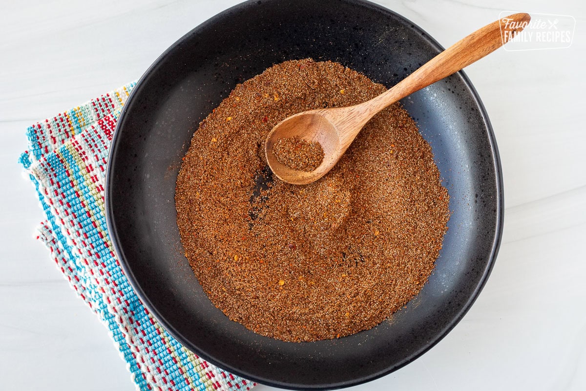 Glass bowl of combined Carne Asada Seasoning with a wooden spoon.