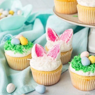 Decorated Easter cupcakes with two designs. One design has bunny ears made with marshmallows and the other has a coconut nest of chocolate Cadberry eggs.