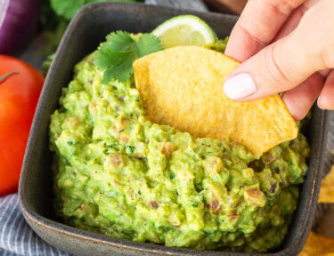 Dipping a tortilla chip into a bowl of guacamole.