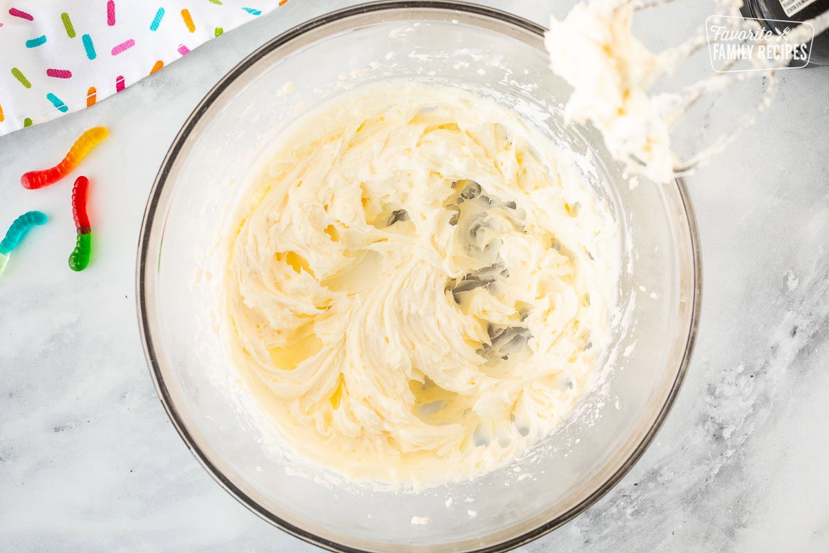 Glass mixing bowl with whipped cream cheese mixture and electric beaters.