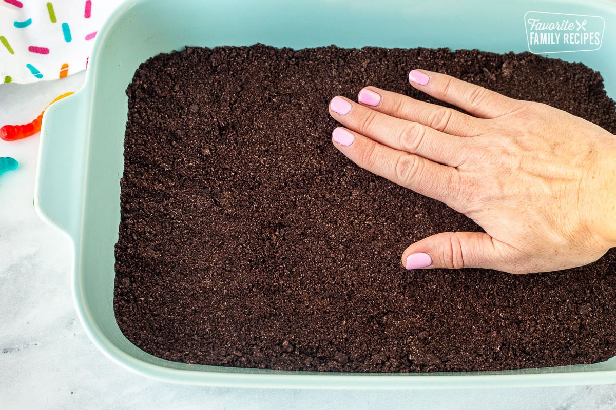 Pressing crushed Oreo cookie crust by hand into a glass 9x13 dish.