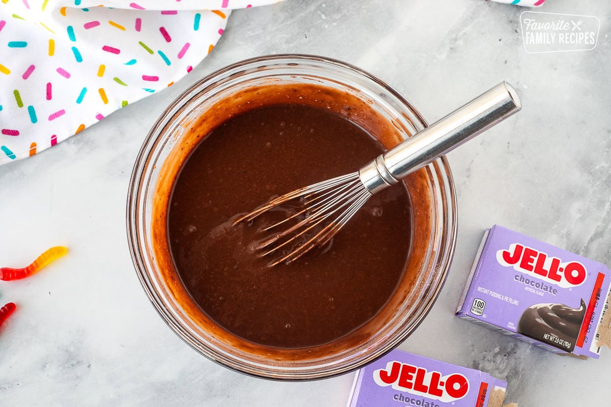 Glass mixing bowl with chocolate pudding and a whisk.