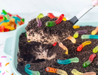 Scoop of dirt cake with gummy worms and a large spoon.