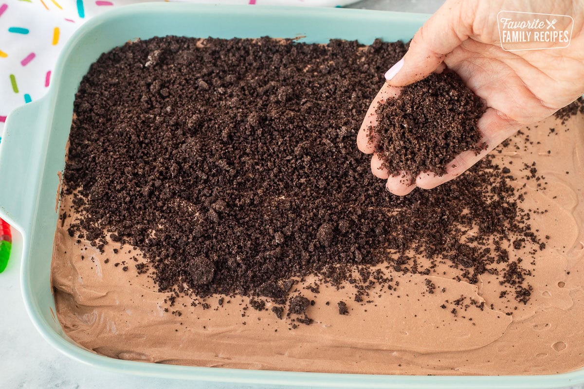 Topping Dirt Cake with crushed Oreo cookies by hand.