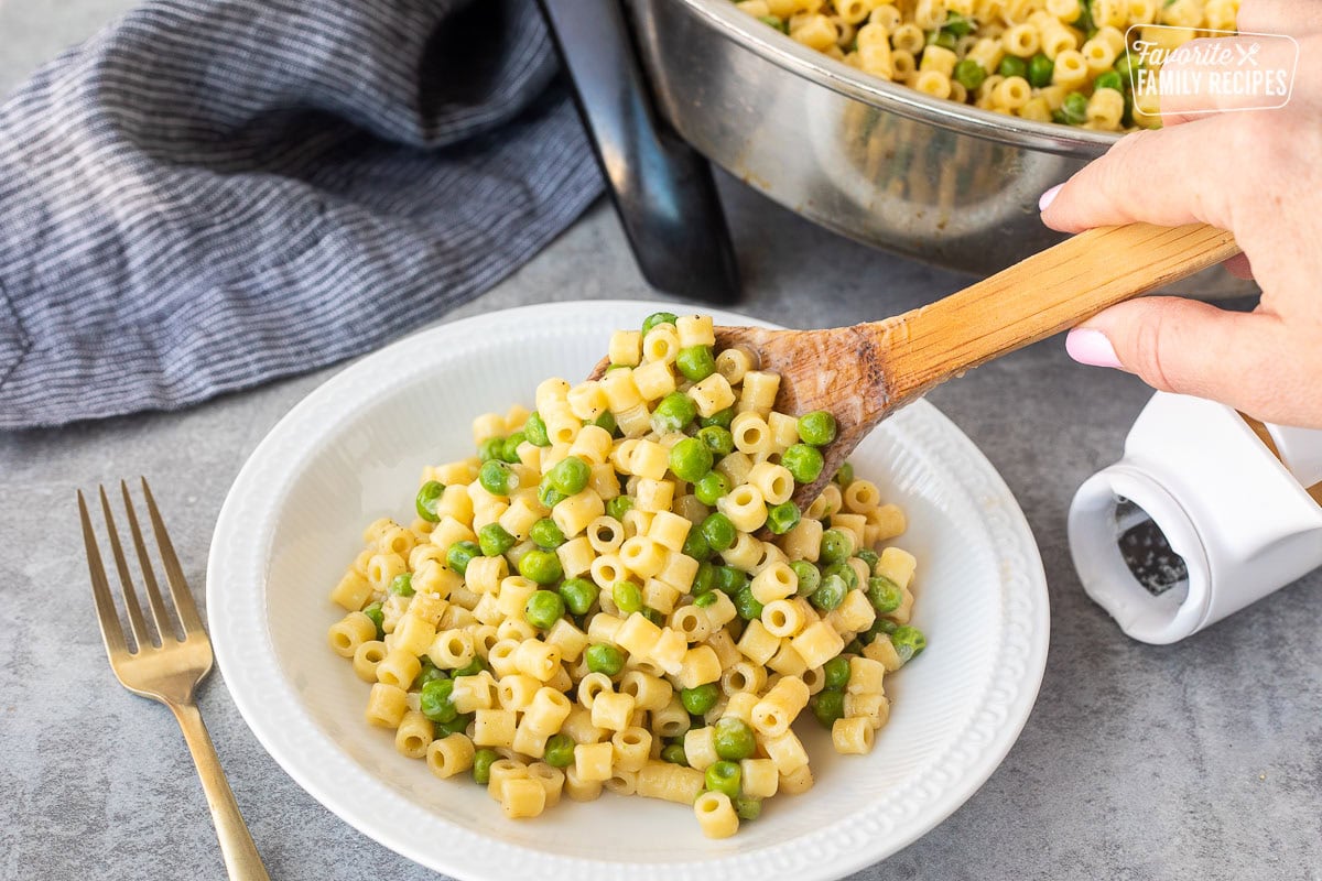 Serving pasta with peas on a plate with a wooden spoon.