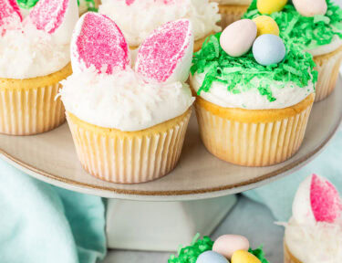 Easter Cupcakes on a cake stand shaped like bunnies and nests with chocolate Cadbury eggs.