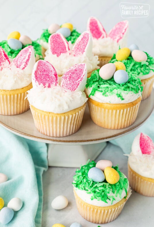 Easter Cupcakes on a cake stand shaped like bunnies and nests with chocolate Cadbury eggs.