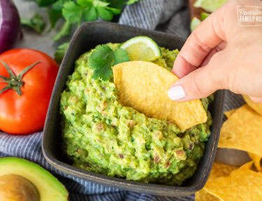 Dipping a corn tortilla chip into a bowl of freshly made guacamole.