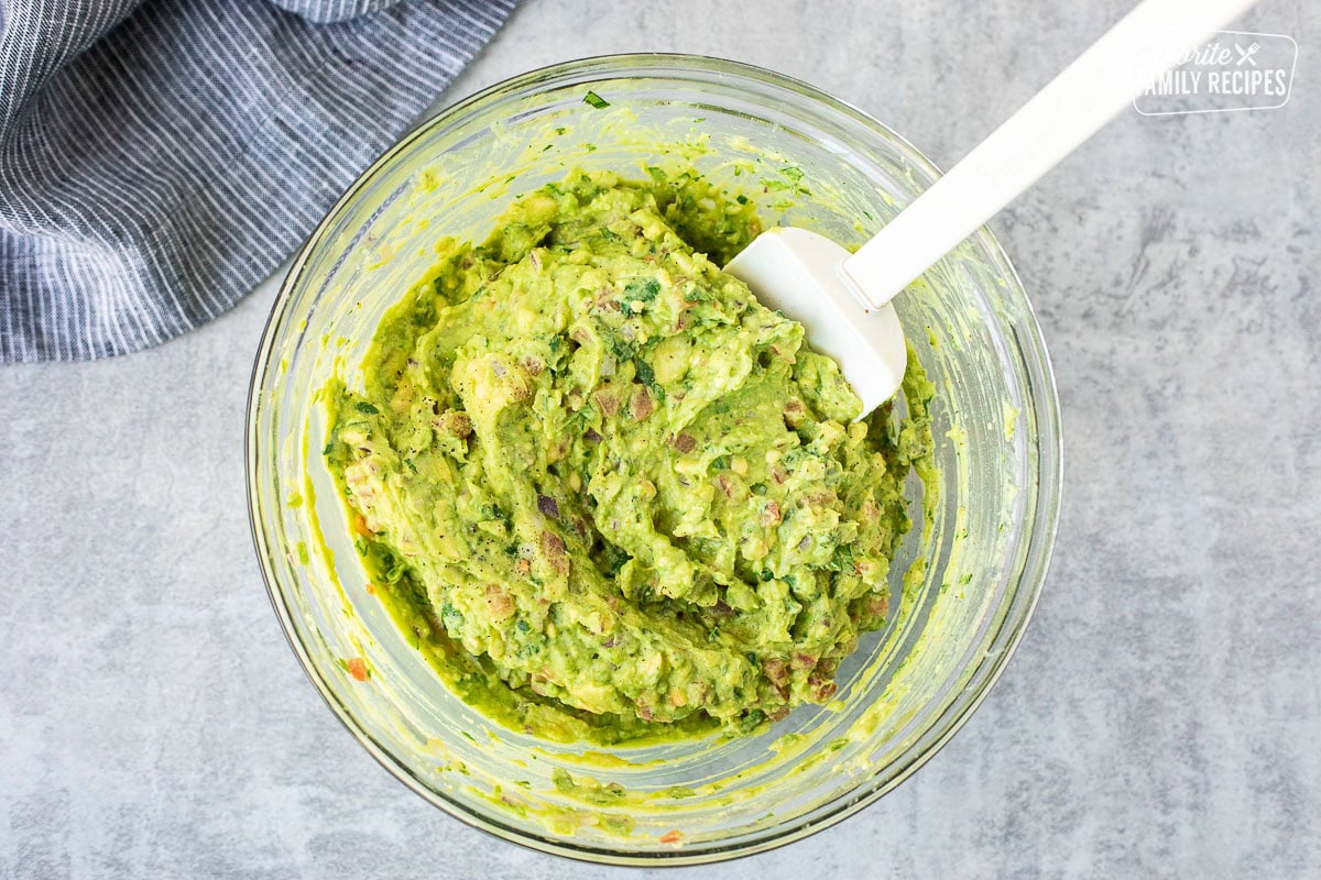 Mixed guacamole in a glass mixing bowl with a spatula.