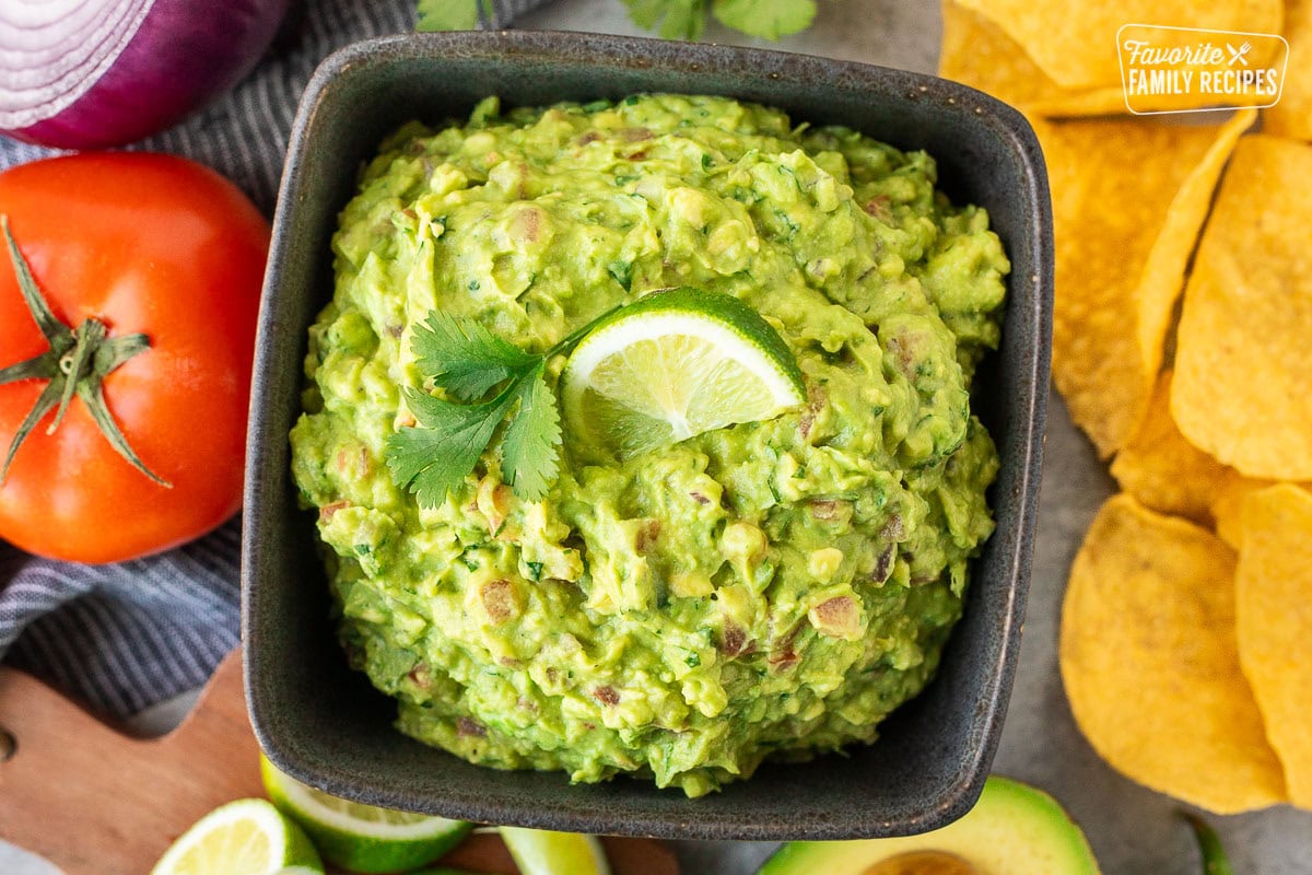 Bowl of guacamole with tomato, cilantro, lime juice, red onion and jalapeño.