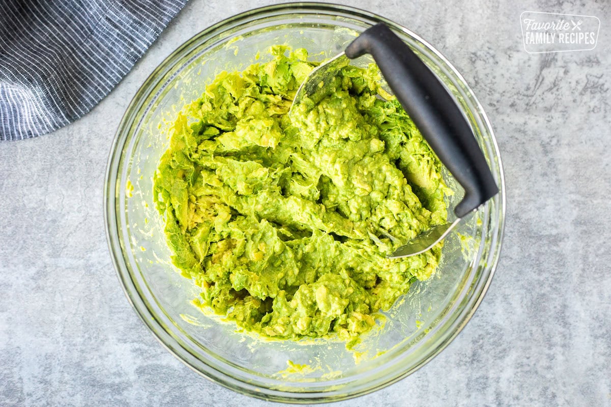 Glass mixing bowl with mashed avocados.