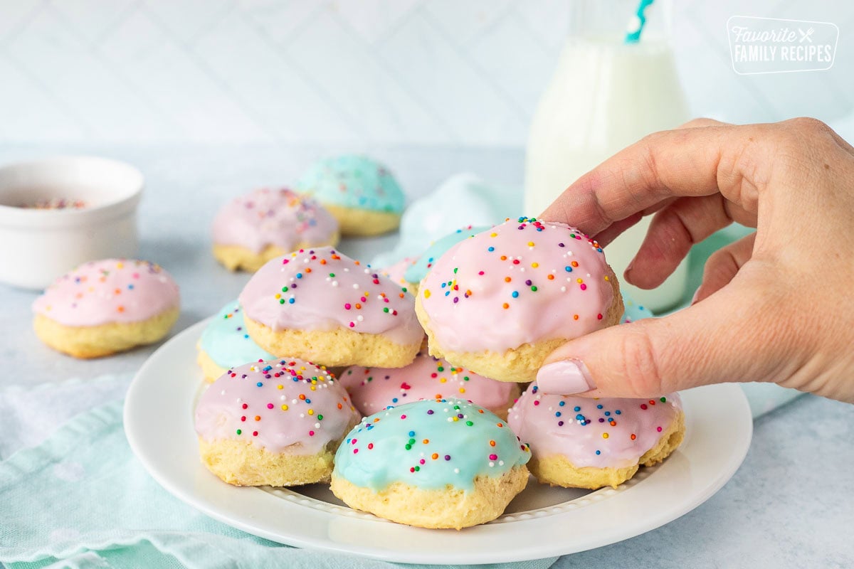 Picking up a pink Italian Easter cookie from a plate of cookies.